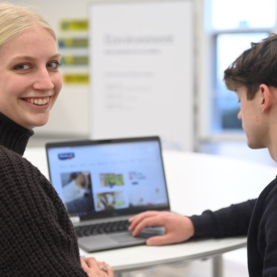 Auszubildender und Mitarbeiterin stehen gemeinsam vor einem Laptop